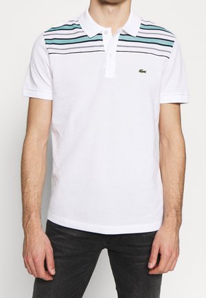 Biała koszulka polo z poziomymi niebieskimi i zielonymi paskami na piersi, krótkie rękawy, kołnierzyk oraz małego zielonego logo po lewej stronie.