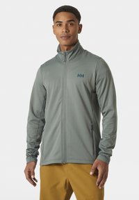 Chaqueta gris claro con cremallera, cuello alzado, tela texturizada, dos bolsillos laterales y un pequeño logotipo en la parte superior del pecho.