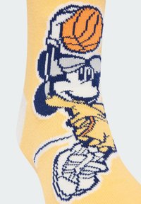 Žltá bavlnená ponožka s tkanou grafikou postavy držacej basketbal, doplnená modrými a oranžovými akcentami.