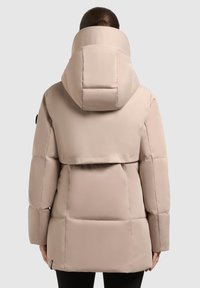 Light beige puffer jacket featuring a high collar and oversized hood, quilted design, and a back flap with a subtle logo detail.