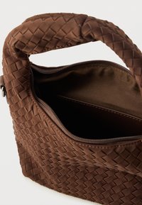 Sac à main brun tissé avec une surface texturée, une poignée arrondie et une ouverture zippée dévoilant une doublure intérieure uni.