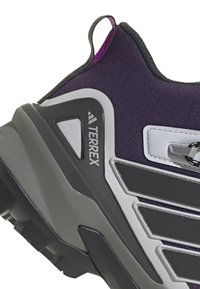 Chaussure de randonnée violette et grise avec une tige en tissu texturé, des accents en plastique, une semelle robuste et une languette au talon pour un enfilage facile.