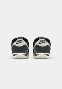 Nike sko med en sort overdel, grå ruskindsdetaljer, en rund tå og en hvid struktureret gummisål med et trekantet slidbanemønster.