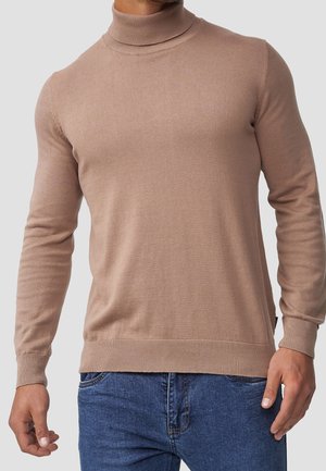 Beiger langärmeliger Rollkragenpullover, getragen mit blauer Jeans an einer Person mit sichtbarem Oberkörper und Armen, neutraler grauer Hintergrund.
