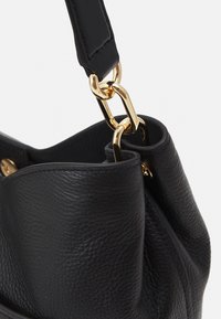 Czarna skórzana torebka o teksturowanej powierzchni, z złotym metalowym łańcuszkiem oraz regulowanym paskiem. Kształt jest miękki i zmięty.