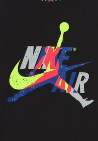 Mustat T-paita, jossa on värikäs graafinen Jumpman-logo, ja kirkkaat neonkeltaiset, siniset ja punaiset tekstit, jotka sanovat "NIKE AIR."