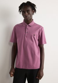 Kratkās piedurknes polo krekls lavandas krāsā ar trīs pogām, izšūts logo uz krūšu daļas un gluda kokvilnas auduma.