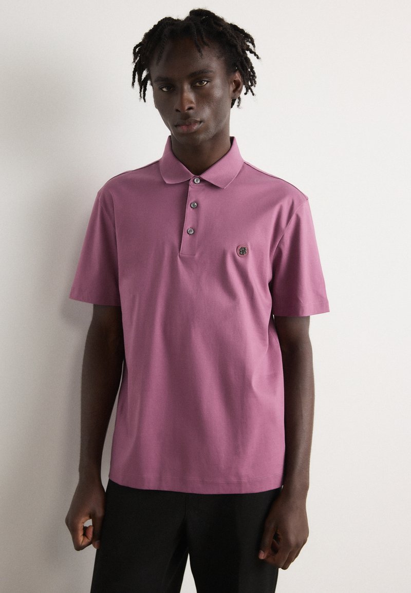 Kratkās piedurknes polo krekls lavandas krāsā ar trīs pogām, izšūts logo uz krūšu daļas un gluda kokvilnas auduma.