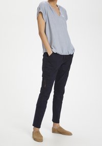 Ljusblå linneskjorta med djup V-ringning, tillsammans med marinblå cargobyxor med sidofickor och tapered benform. Bruna slipskor.