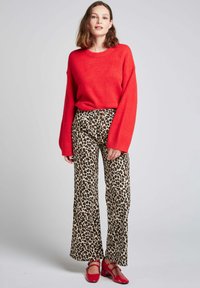 Un pull surdimensionné rouge, un pantalon large à imprimé léopard et des chaussures à talons carrés rouges. Texture douce et motif animal audacieux.