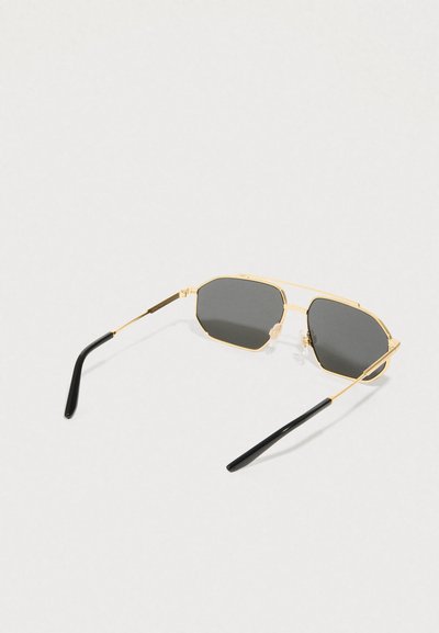 Γυαλιά ηλίου με χρυσή κορνίζα, σκούρους εξαγωνικούς φακούς και μαύρες άκρες σε λεπτούς βραχίονες, απεικονισμένα σε ανοιχτό φόντο.