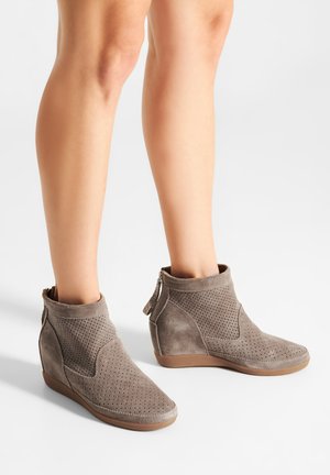 Stivaletti alla caviglia in suede grigio con design perforato, tacco a zeppa, punta arrotondata e cerniere laterali per la chiusura. Superficie testurizzata e dettagli lisci.