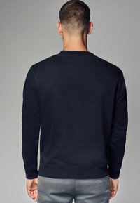 Svart sweatshirt i mjukt tyg med rund halsringning och ribbade ärmslut och fåll. Enkelt design utan synliga mönster eller grafik.