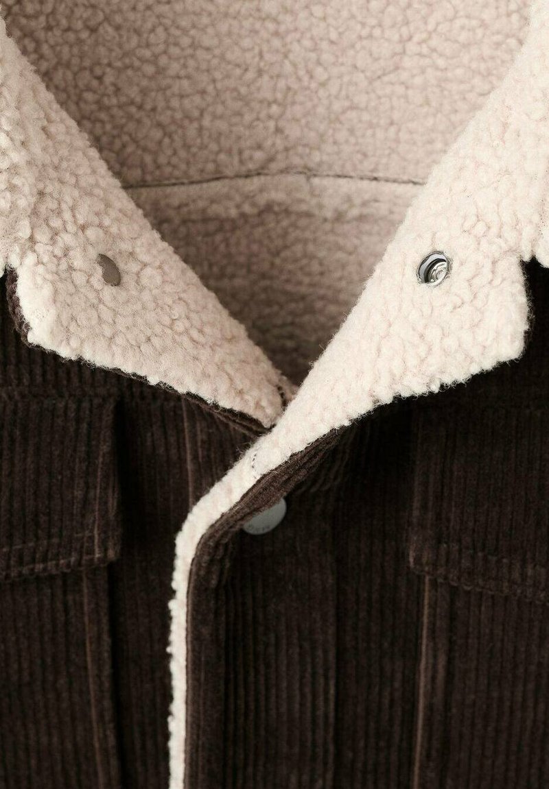 Giacca in corduroy marrone con colletto in sherpa crema, caratterizzata da bottoni a pressione argentati e una trama a coste, evidenziando contrasto e calore.
