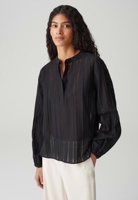 Blusa nera a maniche lunghe con colletto rotondo, tessuto semi-trasparente, righe verticali e chiusura con bottoni sul davanti.