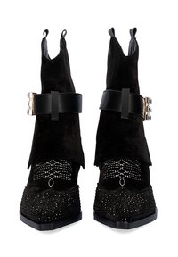 Botas de tobillo de ante negro con punta afilada, que presentan una gruesa correa negra y herrajes plateados, adornadas con elementos brillantes en la parte frontal.