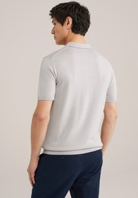 Pelēks īsām piedurknēm polo krekls ar ribotu apkakli un apakšmalu, izgatavots no gludas adītas auduma, redzams no mugurpuses ar vieglu tekstūru.