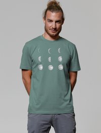 Grünes Baumwoll-T-Shirt mit einem weißen Mondphasen-Grafik. Kurze Ärmel, runder Ausschnitt und lockere Passform. Die Textur ist weich und glatt.