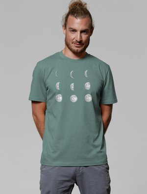 Groene katoenen t-shirt met een grafische weergave van maanfases in het wit. Korte mouwen, ronde halslijn en een ontspannen pasvorm. De textuur is zacht en glad.