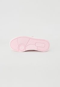 Semelle de sneaker rose clair avec une surface en caoutchouc texturé, des motifs concentriques et un logo circulaire détaillant sur le côté.