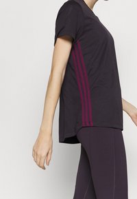 Černé sportovní tričko s krátkými rukávy, se třemi vertikálními fuchsiovými pruhy po straně a uvolněným střihem.