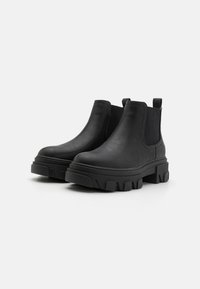 Botas Chelsea negras hechas de material sintético suave, con una suela gruesa y estriada, paneles laterales elásticos y tiradores para facilitar su uso.