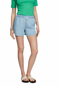 Pantaloni corti azzurri chiari realizzati in un tessuto morbido, con vita elasticizzata e cordino. Abbinati a una maglietta verde e sandali beige.