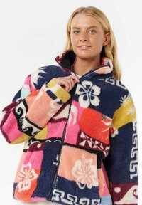 Veste en polaire colorée présentant un mélange de motifs, y compris des fleurs et des formes géométriques, avec un col haut et une fermeture éclair.