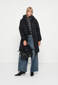 Manteau noir matelassé avec capuche, associé à une chemise grise à carreaux, un jean bleu à pattes d'éléphant et des chaussures à talons noires. Comprend un sac noir texturé.