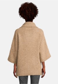 Beżowy, teksturowany, oversize'owy płaszcz z kołnierzem typu szal, rękawami o długości trzech kwart, i prostym dołem, pokazany z tyłu.