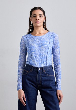 Light blue long-sleeve top with a floral pattern, featuring a round neckline and fitted design, paired with dark blue high-waisted jeans.