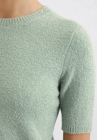 Maglione a maniche corte di colore verde chiaro, realizzato in materiale testurizzato con una finitura morbida e colletto a coste.