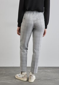 Grijze ruitbroek met een getailleerd ontwerp en elastische tailleband, gecombineerd met witte sneakers met beige accenten en een gestructureerde zool.