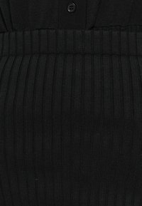 Černé pletené šaty s ribovanou strukturou, přiléhavým pasem s plisováním a knoflíkovým zapínáním poblíž výstřihu.