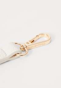 Vit strukturerad läderrem med ett guldfärgat metallspänne som har ingraverat "VALENTINO." Slät yta med glänsande detaljer.