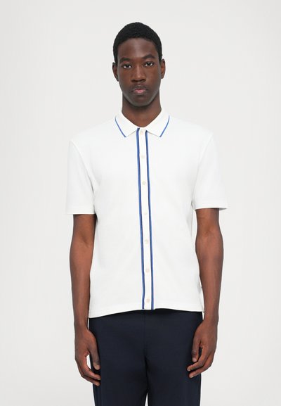 Chemise polo blanche avec une rayure bleue le long des boutons, dotée d'un col classique et de manches courtes. Texture lisse, matériau léger.