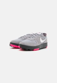 Gray athletic shoes with a mesh and suede upper, white logo, black midsole, and pink outsole accent. Laced design with padded collar.