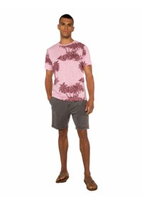 T-shirt rosa chiaro con stampa di palme rosso scuro, abbinata a pantaloni corti grigi e sandali marroni. Design semplice, maniche corte e vestibilità comoda.