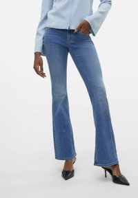 Svetr svetlo modre barve z dolgimi rokavi v kombinaciji z temno modrimi hlačami srednje višine in razširjenimi nogavicami. Hlače imajo subtilno blago bledenje in šivano obrobo vzdolž šivov.