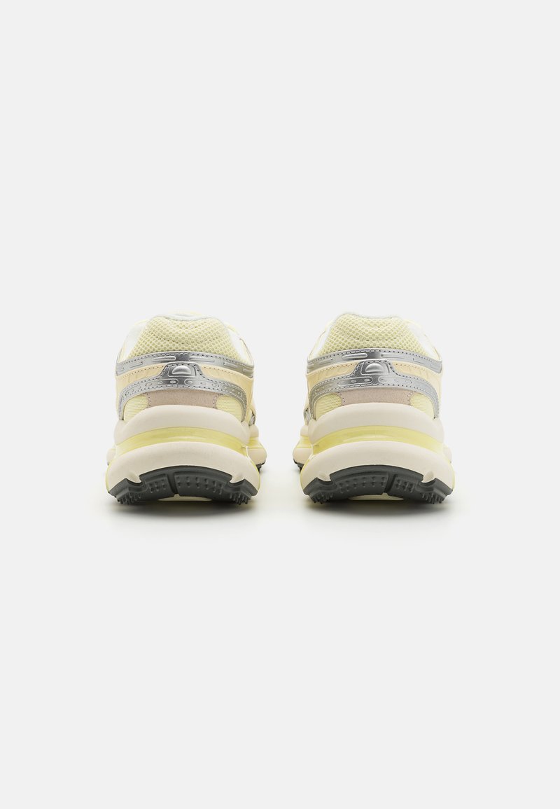 Buty sportowe z siateczkowej i syntetycznej cholewki w kolorze żółtym i kremowym, z metalicznym akcentem w kolorze srebrnym oraz teksturowaną czarną gumową podeszwą.