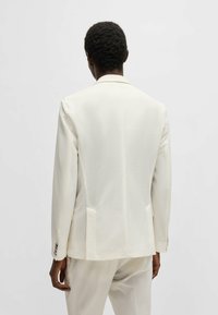 Blazer bianco con texture, dalla vestibilità slim, con rever a punta e doppi spacco. Presenta dettagli con bottoni argentati sui polsini e due tasche posteriori.