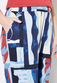 Pantaloni larghi e multicolori caratterizzati da un motivo grafico in blu, blu scuro e rosso, con vita elasticizzata e tasche laterali.