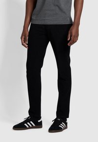 Schwarze Cordhosen mit einem Slim Fit, die eine strukturierte Oberfläche aufweisen, seitliche Taschen haben und mit schwarzen Sneakers mit weißen Streifen getragen werden.