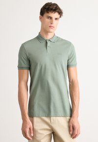 Grønn polo-skjorte laget av et mykt stoff. Har en klassisk krage, tre knapper, korte ermer og en liten logo på brystet.