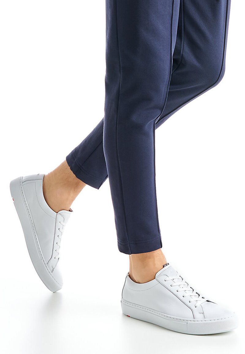 Witte leren sneakers met een gladde textuur, voorzien van een ronde neus, veters aan de voorkant en een rubberen zool. Gecombineerd met marineblauwe joggerbroek.