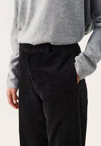 Pantalon en velours côtelé noir avec une texture côtelée verticale, présentant une coupe droite et des poches, associé à une chemise à manches longues gris clair.