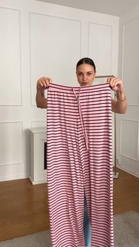 Roza prugasta hlače z vrvico v pasu, ki imajo vertikalne črne črte. Narejene so iz mehke, raztegljive tkanine; brez opaznih kovinskih detajlov.