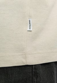 T-shirt en coton beige clair avec un ourlet droit et une petite étiquette Jack & Jones tissée sur le côté. Associe avec un tissu en denim foncé en dessous.
