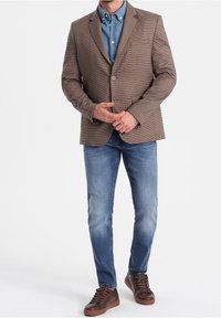 Brązowa marynarka w wzory na jasnoniebieskiej koszuli, zestawiona z niebieskimi dżinsami i brązowymi trampkami. Posiada dopasowany krój i dwie przednie kieszenie.