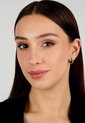 Primo piano del viso di una donna con capelli castano scuro lisci, trucco naturale e un orecchino d'argento con un design curvato.